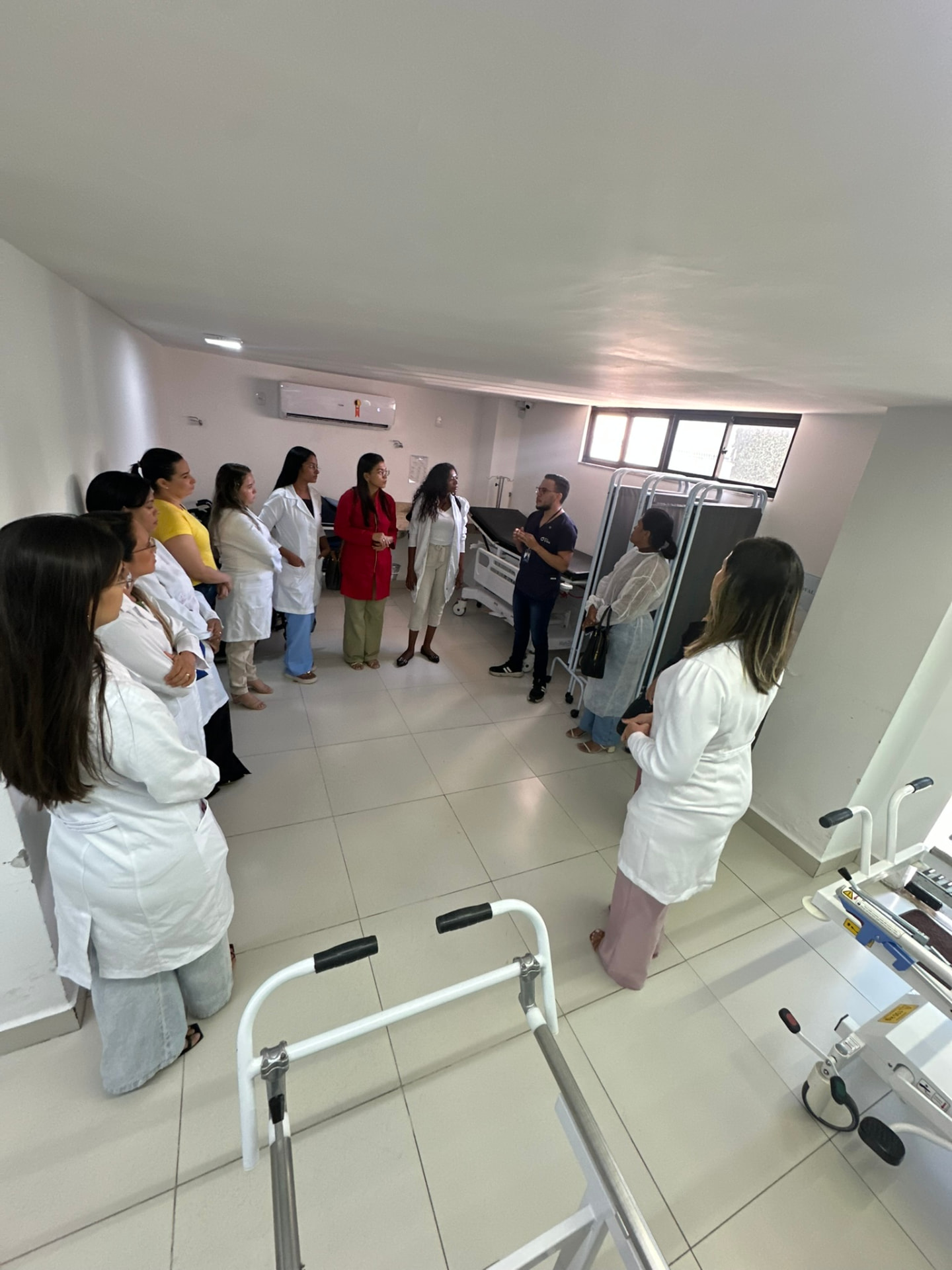 Alunas de jaleco branco acompanhando orientação do professor em sala de cuidados com feridas